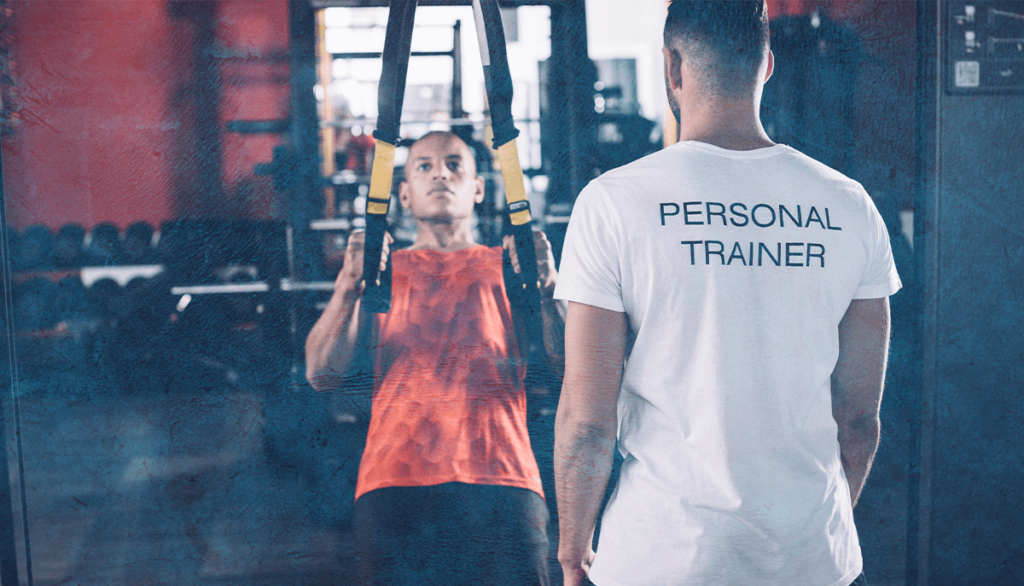 Персонален фитнес инструктур наблюдава свой клиент, докато той изпълнява упражнение.